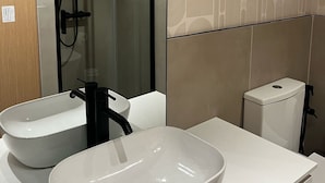 Ett modernt badrum med ett stort ovalt handfat, en duschkabin i glas och en toalett.