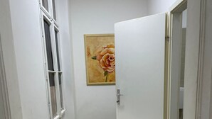 Un corridoio stretto con pavimento piastrellato, una porta bianca e una finestra con infissi bianchi.