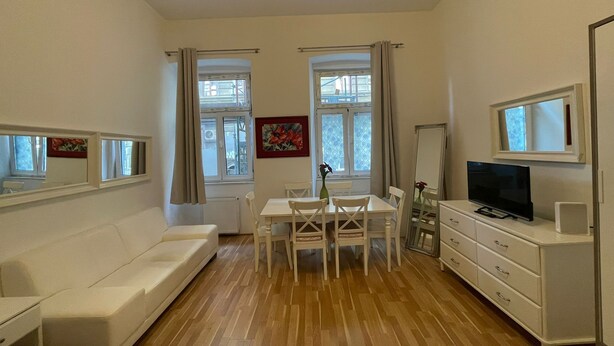 Una camera moderna e luminosa, con divano, tavolo da pranzo con sedie, televisore e comò.