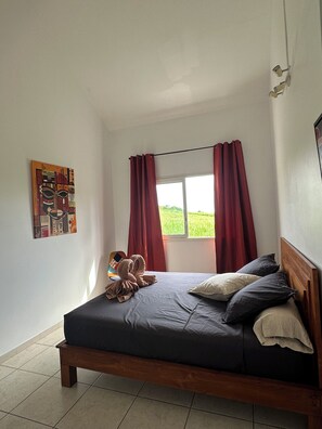 Um quarto com cama, janela com cortinas, um quadro na parede e cabeceira de madeira.