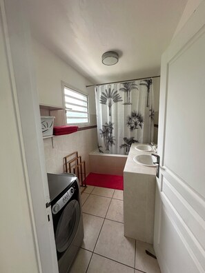 Uma casa de banho compacta com máquina de lavar roupa, cortina de chuveiro com motivos de palmeiras e duas pias.
