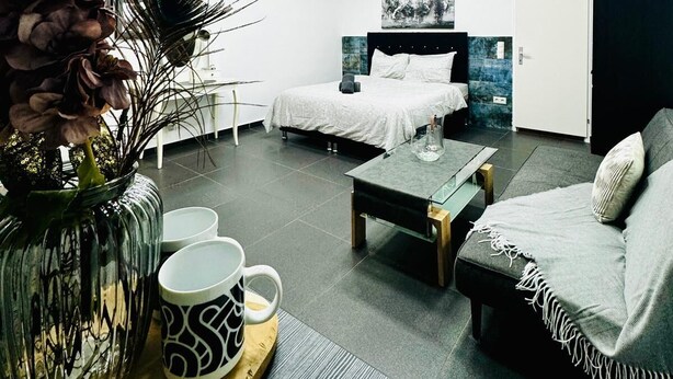 Ein modernes Hotelzimmer mit einem großen Bett, einer Couch, einem Couchtisch und einer dekorativen Vase mit Blumen.