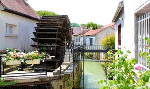Een klassieke watermolen met een houten constructie, omringd door woongebouwen en een smal kanaal.
