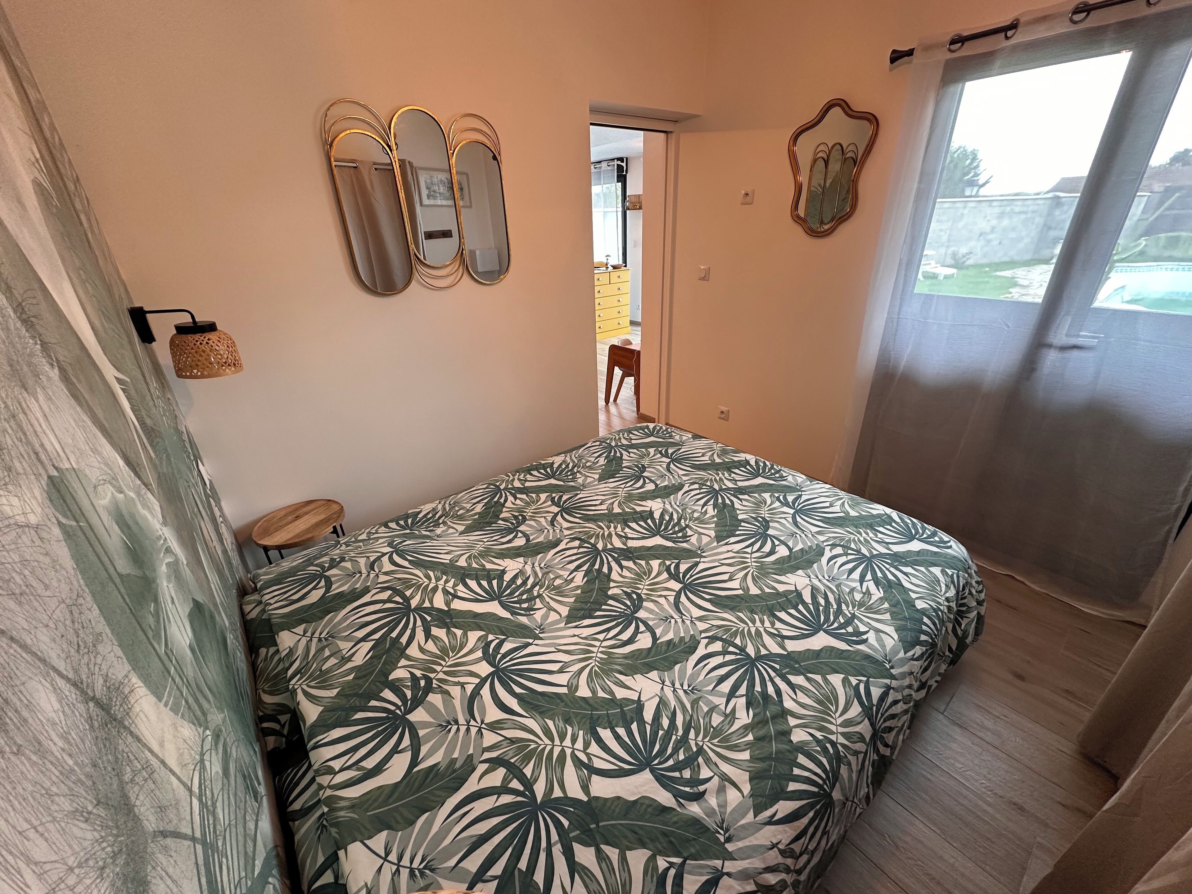 Un dormitorio con cama, espejo, lámpara y vistas al exterior.