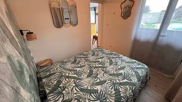 Un dormitorio con cama, espejo, lámpara y vistas al exterior.