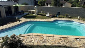 Une piscine aux parois recouvertes de carrelage en pierre, entourée d’un mur en pierre, et un espace patio aménagé avec du mobilier d’extérieur.