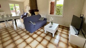 Un salon avec un canapé bleu, une table basse blanche, un téléviseur posé sur un meuble et une grande cheminée.