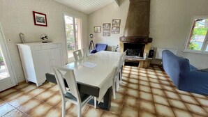 Un espace repas avec une table blanche, des chaises et un coin cuisine équipé d’une cuisinière.