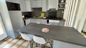 Une cuisine compacte avec des meubles gris, un îlot central doté de deux tabourets de bar, un four encastré et une cuisinière.
