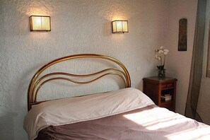 Ein Bett mit Kopfteil, zwei Wandlampen, ein kleiner Nachttisch mit Blumenvase und ein gerahmtes Bild an der Wand.