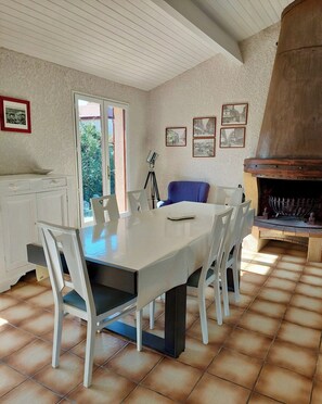 A dining area with a table and chairs, a tripod lamp, framed pictures on the wall, and a fireplace. - Holiday house close to the ocean G0238 (Lacanau Ocean)