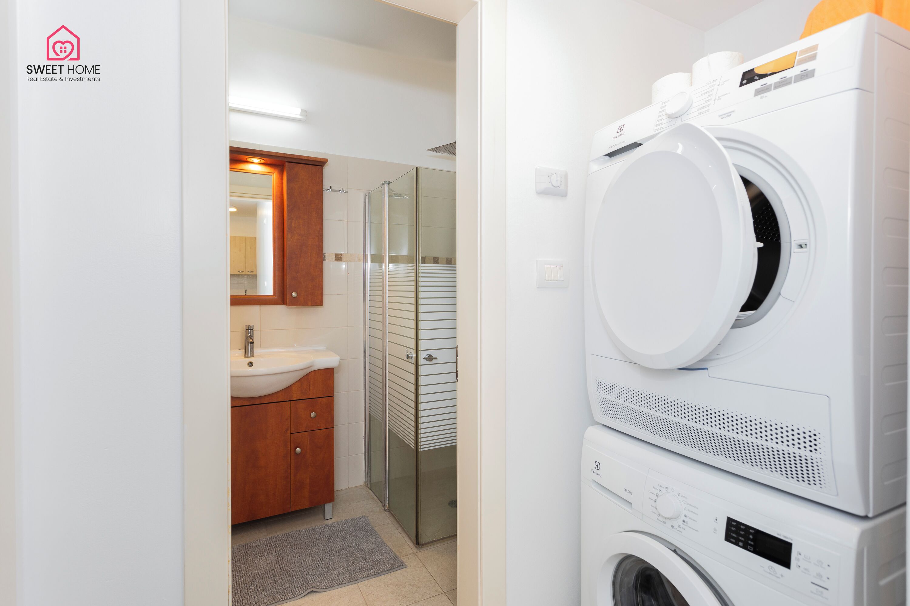 A modern bathroom with a sink, mirror, and stacked washing machines.