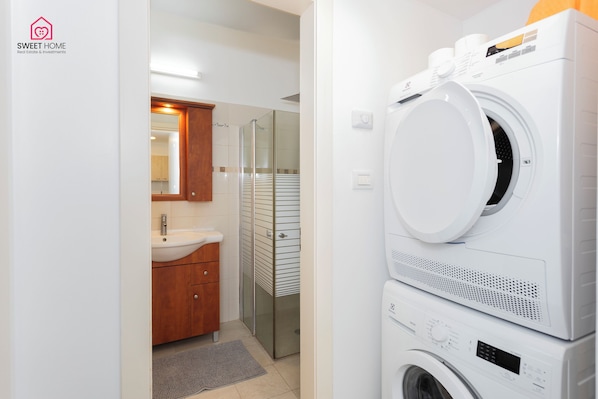 A modern bathroom with a sink, mirror, and stacked washing machines. - Quiet Oasis in the Center (Netanya)
