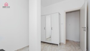 A modern, minimalist room with white walls and a tiled floor. It includes a wardrobe with mirrored doors and a door leading to another room. - Quiet Oasis in the Center (Netanya)