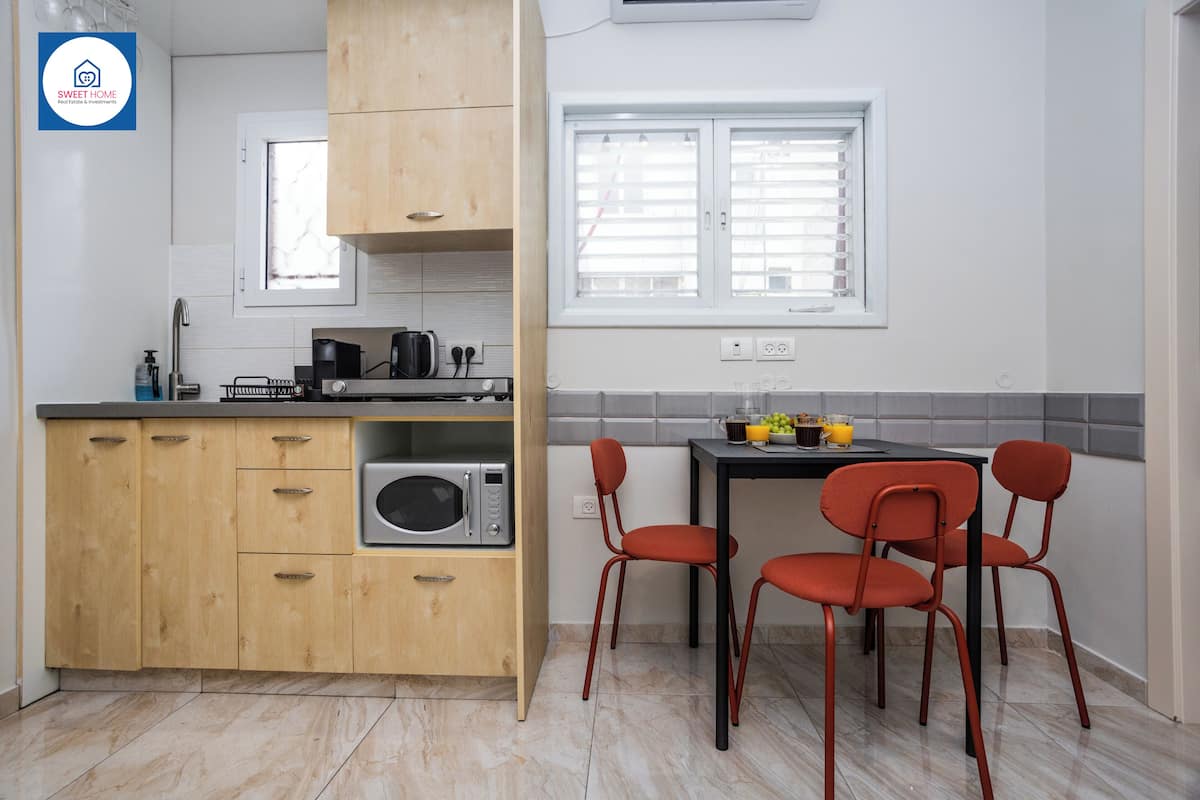 A compact kitchen with wooden cabinets, a microwave, a gas stove, and a dining area with two red chairs.