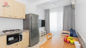 A modern kitchen with a refrigerator, microwave, and gas stove. There is a dining table with fruit and cups. - Quiet Oasis in the Center (Netanya)