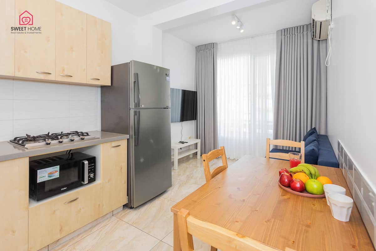 A modern kitchen with a refrigerator, microwave, and gas stove. There is a dining table with fruit and cups.