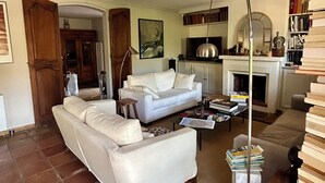 A living room with a white sofa, a coffee table, and a fireplace. There are bookshelves and a lamp. - Charming house with direct view of Sainte Victoire and Picasso castle. (Vauvenargues)