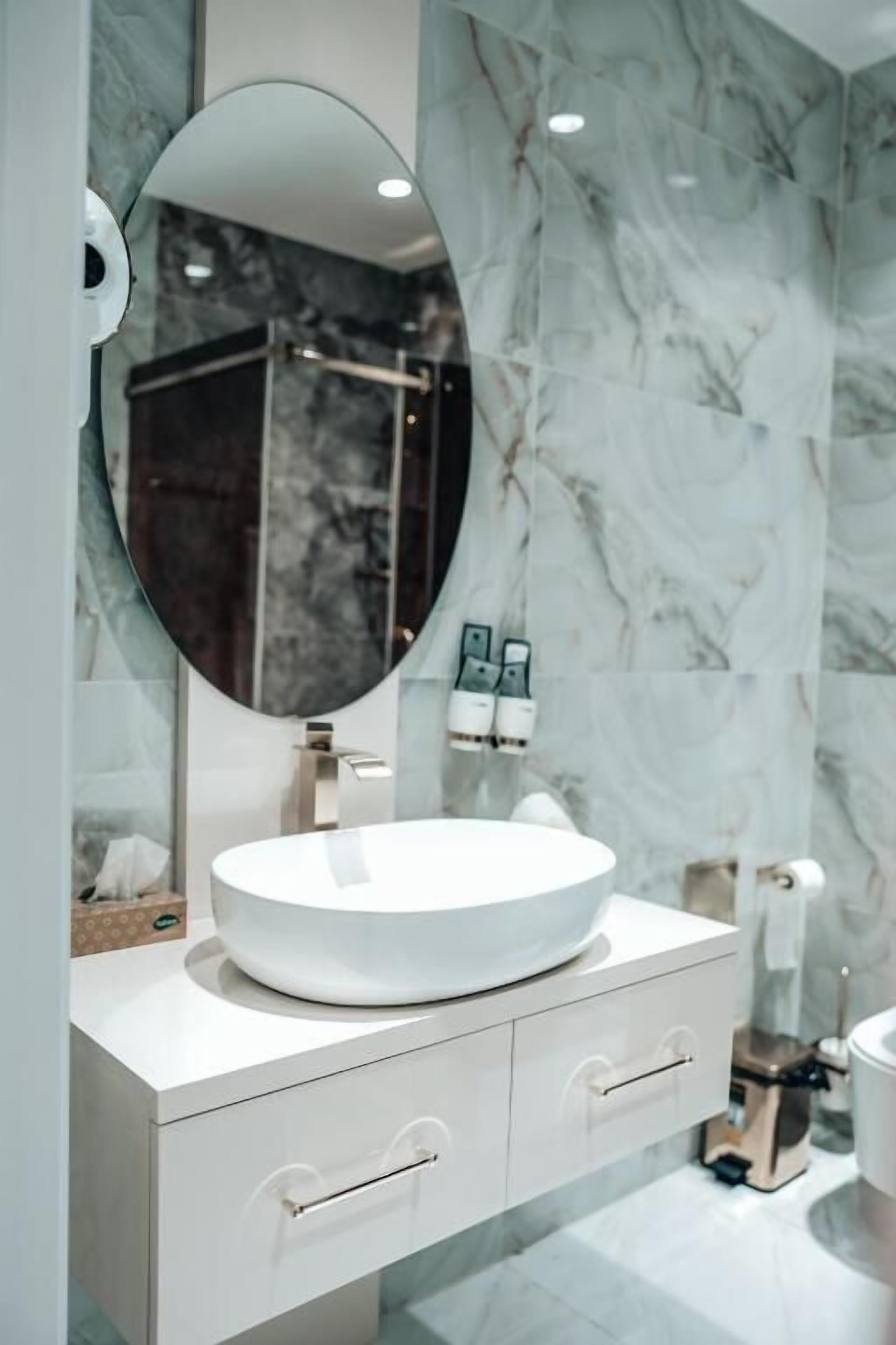A modern bathroom with a white vanity, a round mirror, and marble walls.