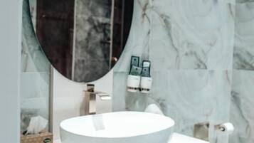 A modern bathroom with a white vanity, a round mirror, and marble walls.
