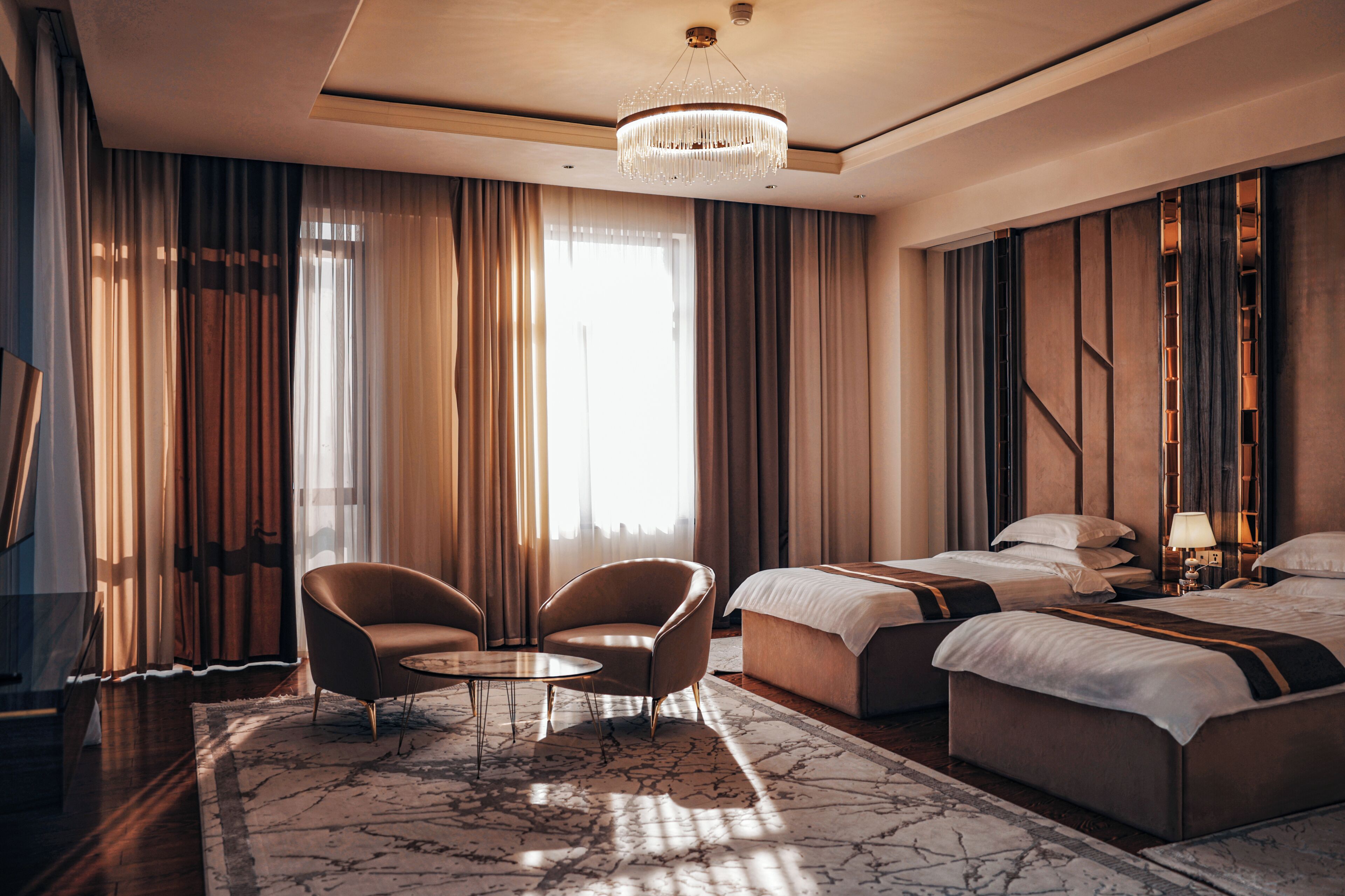 A hotel room with a large bed, two armchairs, a small table, and a chandelier.