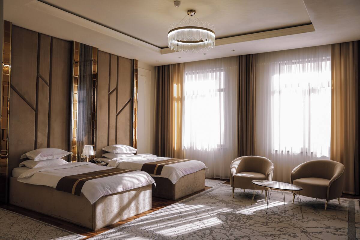 Ein Hotelzimmer mit zwei Betten, einer Sitzecke mit Tisch und großen, mit Vorhängen versehenen Fenstern.