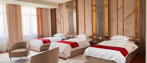 A hotel room with three beds, a sitting area with a chair, and a large window with curtains.