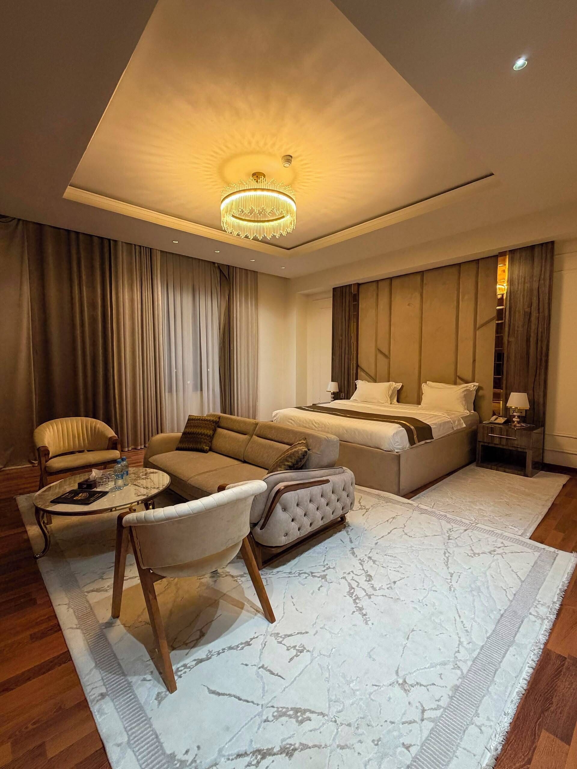 Quarto de hotel moderno com uma cama grande, um sofá, uma mesa de centro e um candelabro.