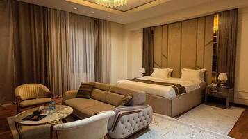 Quarto de hotel moderno com uma cama grande, um sofá, uma mesa de centro e um candelabro.