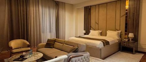Quarto de hotel moderno com uma cama grande, um sofá, uma mesa de centro e um candelabro.