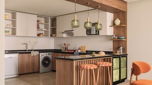 Eine moderne Küche mit Holzausstattung, einer zentralen Kochinsel mit Barhocker, einer Waschmaschine und einer Mikrowelle.