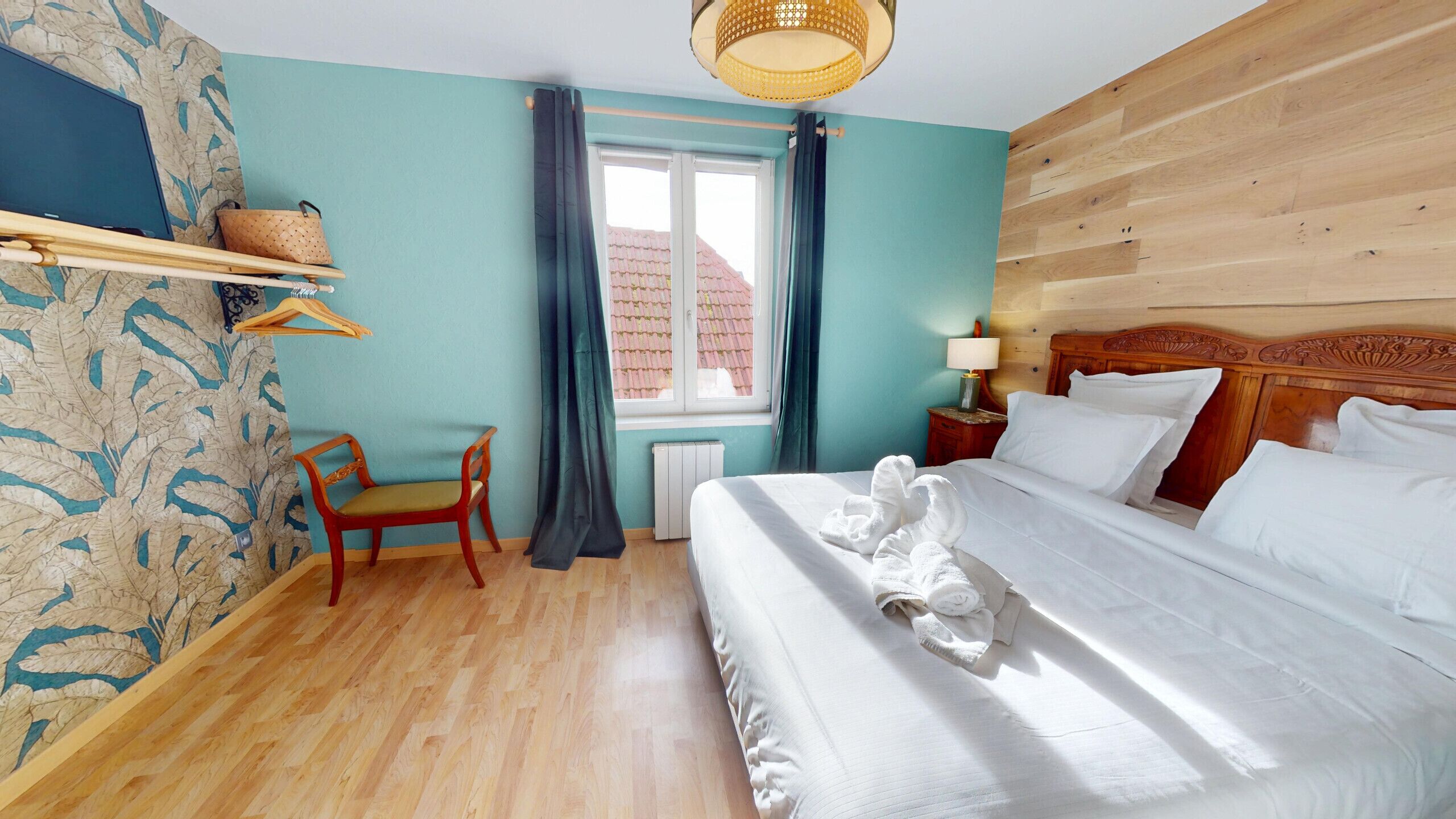 A hotel room with a wooden headboard, a bed with white linens, a chair, a window with curtains, and a wall with a leaf pattern.