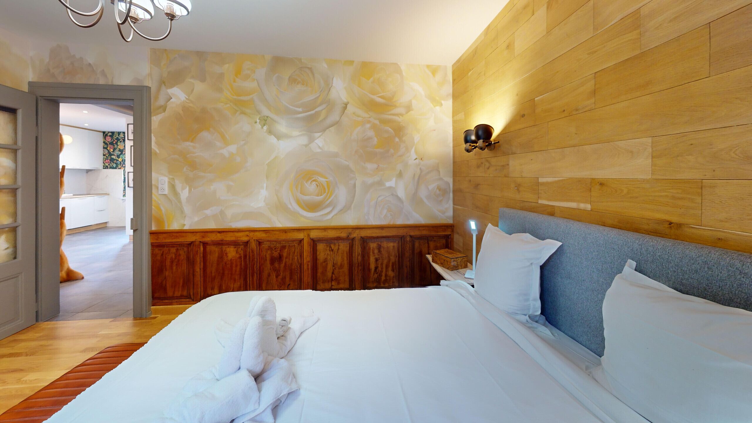 A hotel room with a wooden headboard, a large bed with white linens, a wall with a floral mural, and a wooden floor.