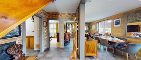 Un vaste espace dédié à la salle à manger, avec une table et des chaises en bois, donnant sur la cuisine, et un escalier menant à un autre niveau.