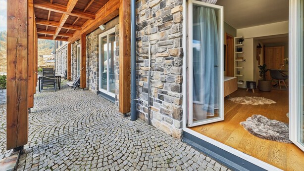 A stone exterior with wooden beams, a covered patio, and a view into the interior. - Na Kovárně by Interhome (Pec pod Snezkou)