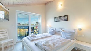 Ein Schlafzimmer mit einem großen Bett, einem Sessel, einem Nachttisch und Blick durch eine Glastür.