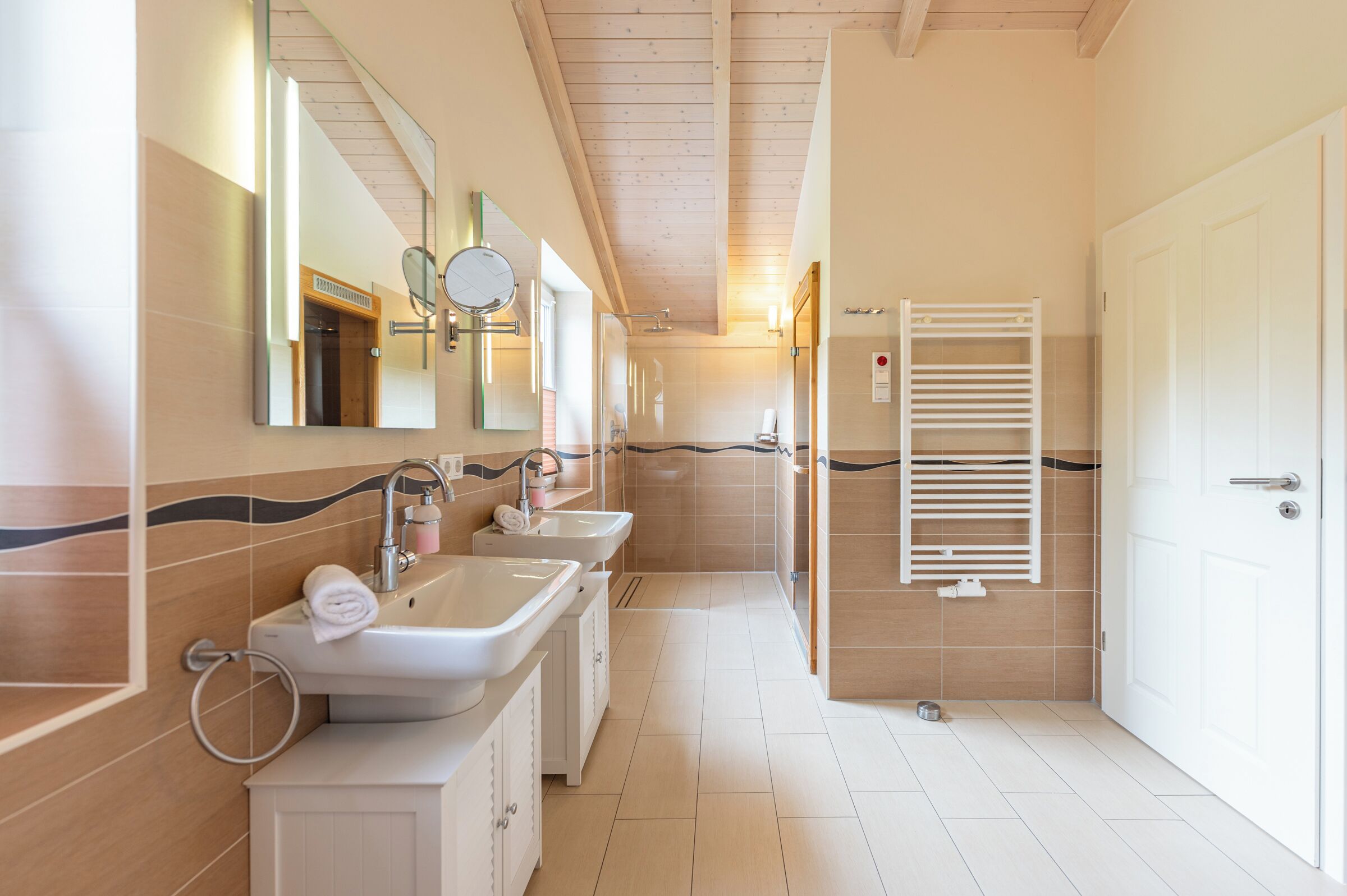 Ein modernes Badezimmer mit zwei Waschbecken, einer Dusche, einem Handtuchhalter und einem Spiegel.