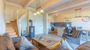 Ein modernes Wohnzimmer mit Treppe, Holzboden und Essbereich, im Hintergrund eine Küche.