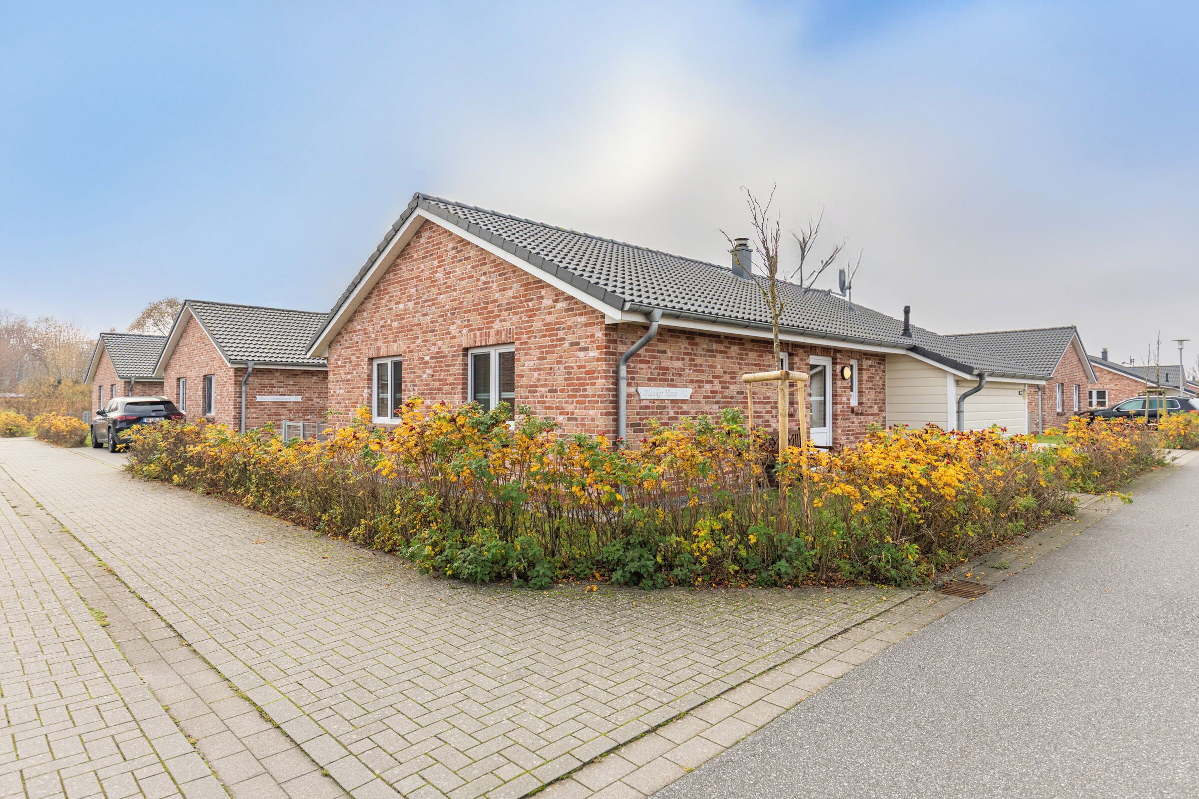 A row of brick houses with a paved driveway and a flower bed in front.