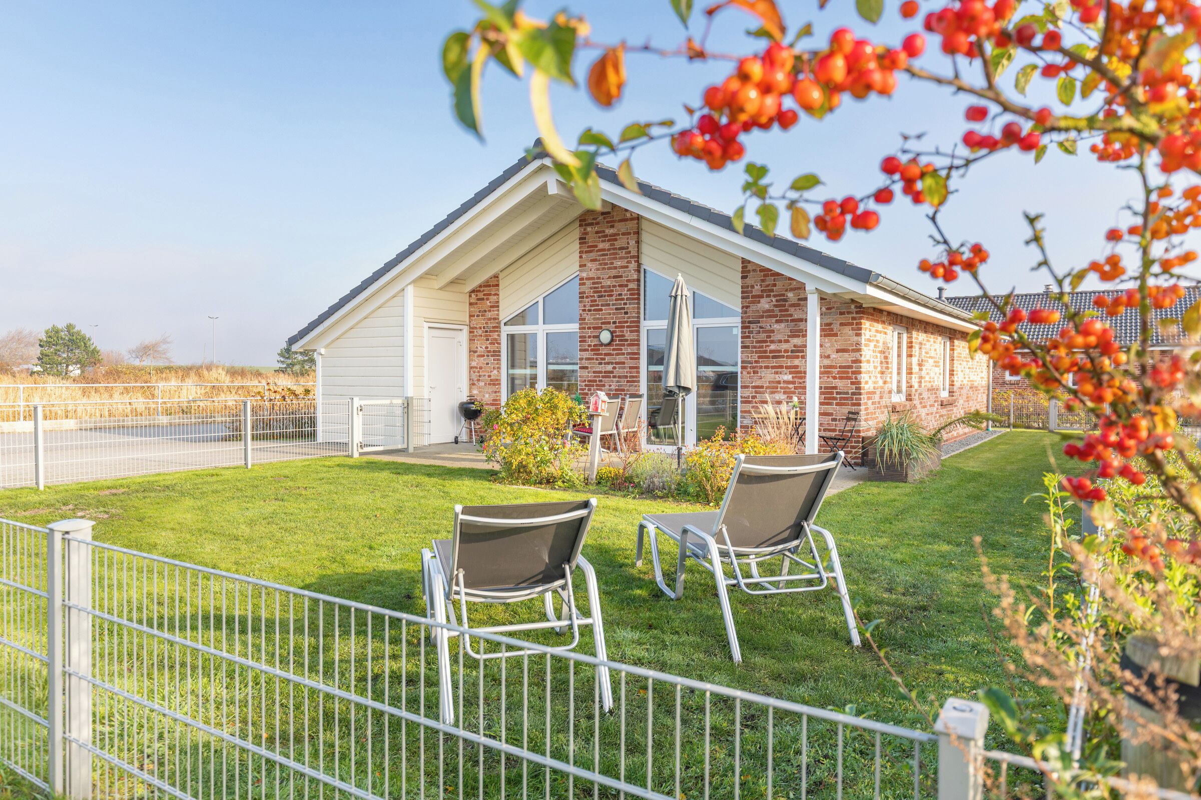 A house with a brick exterior, a covered patio with two chairs, and a fenced yard.