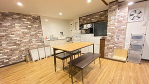 A modern kitchen with a wooden table and bench, a brick accent wall, and a built-in oven. - AkiraHome Haginochaya (Osaka)