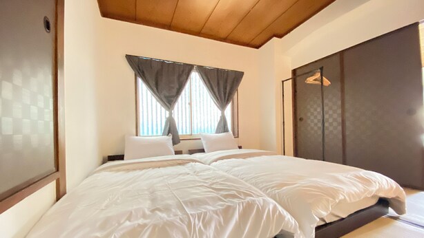 A bedroom with a large bed, a wooden ceiling, and a window with curtains. - AkiraHome Haginochaya (Osaka)