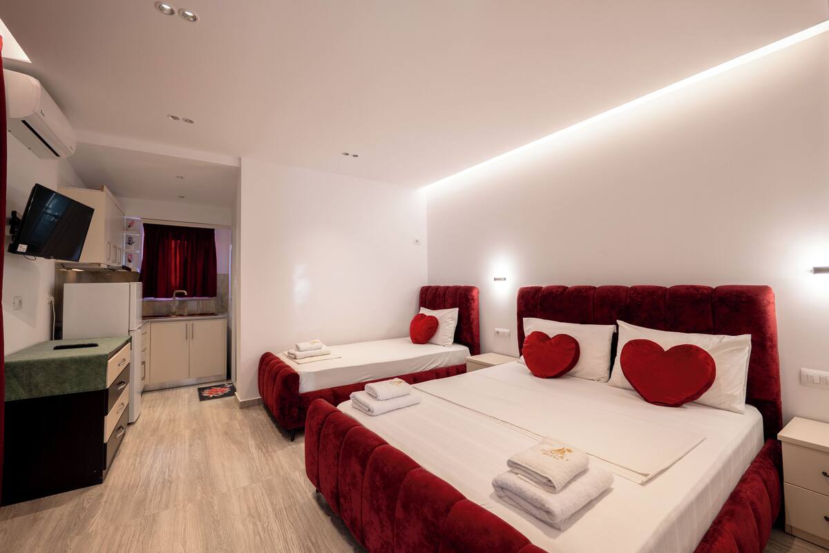 Habitación de hotel con dos camas, televisión, kitchenette y una cortina roja.