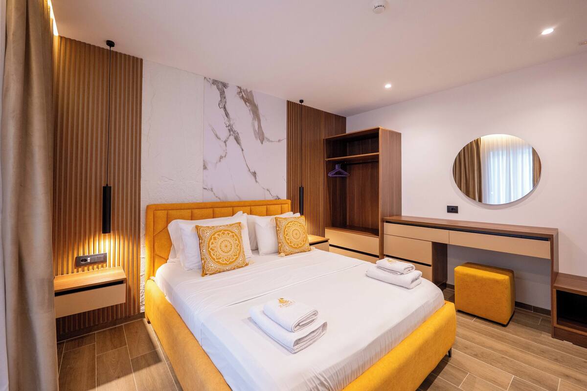 Una habitación de hotel moderna con cama, mesita de noche, armario y un espejo redondo.