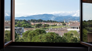 Vista desde una ventana sobre un pueblo con edificios, árboles y montañas al fondo.