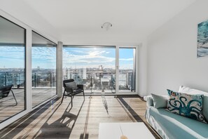 A modern living room with a large sliding glass door leading to an outdoor balcony, a sofa, a coffee table, and a chair. - Loft Fluxus Emden | Delft View (Emden)