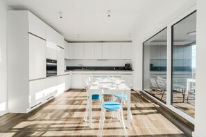 A modern kitchen with white cabinets, a dining table with clear chairs, and a large window. - Loft Fluxus Emden | Delft View (Emden)