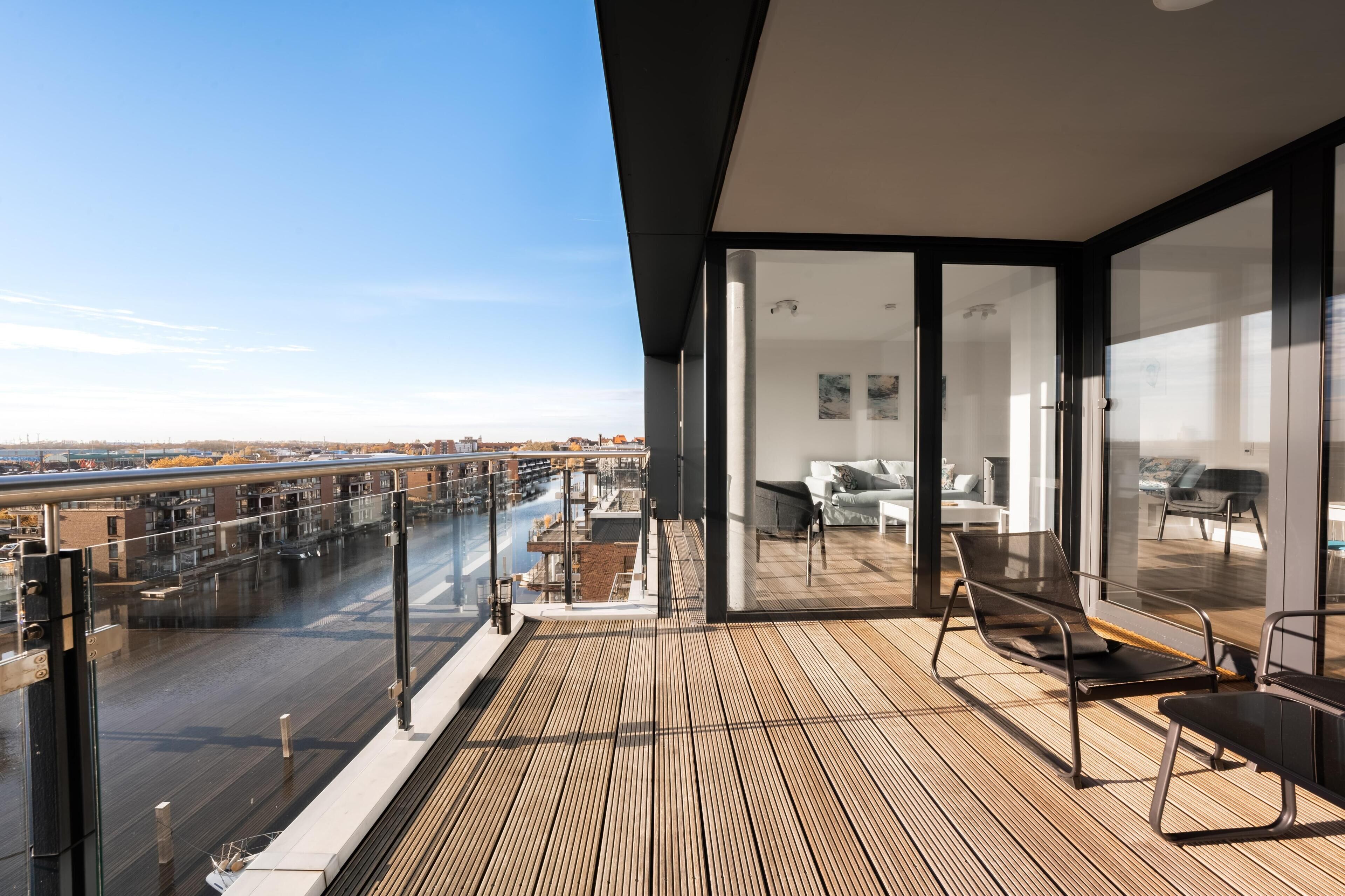 Ein moderner Balkon mit Blick auf die Stadt, eine Glastür, die zu einem Wohnbereich führt, und ein Holzboden.