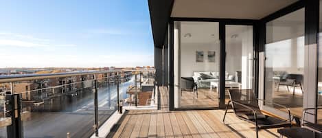 Un balcón moderno con vistas a la ciudad, un ventanal de vidrio que da a una sala de estar y piso de madera.
