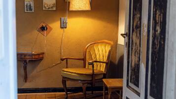 Une pièce comprenant une chaise en bois, une petite table, une lampe fixée au mur et des tableaux encadrés.